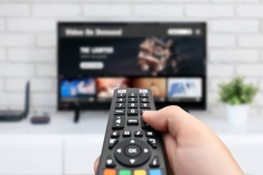 Televizyon izleyen adam, uzaktan kumanda elinde. TV 'de VOD hizmeti