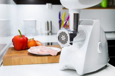 Meat grinder in modern kitchen. Vegetables in background clipart