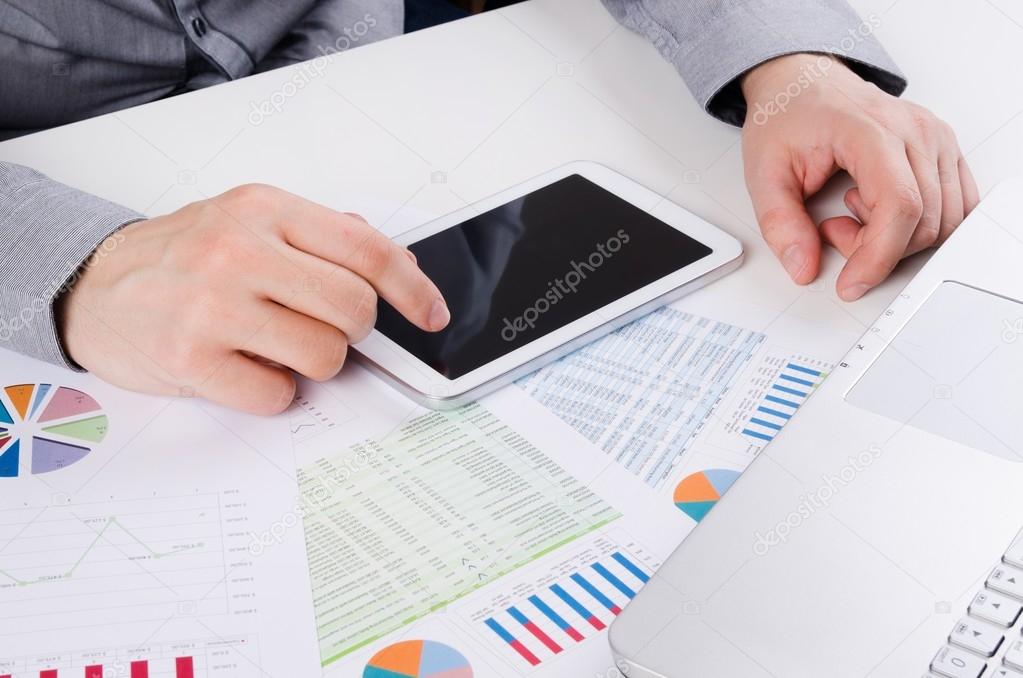 Businessman working with digital tablet. Report charts on desk