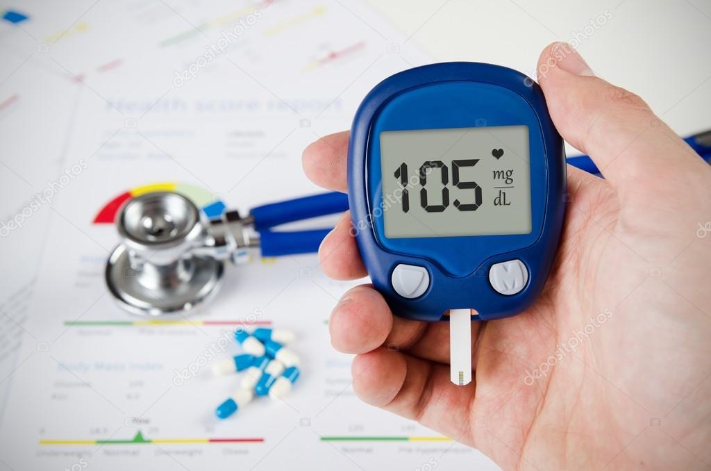 Hand holding glucometer. Stethoscope and pills in background