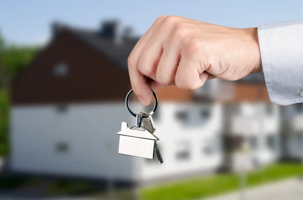 Hombre mano sosteniendo llaves con a nueva casa —  Fotos de Stock