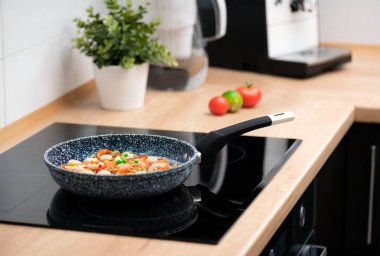 Cooking fresh vegetables in a pan in modern kitchen, induction stove