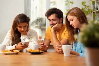 Mutfakta oturuyor ve üstünde onların telefon izlerken arkadaşlar. Internet'te gezinme ve teknoloji bağımlılığı kavramı