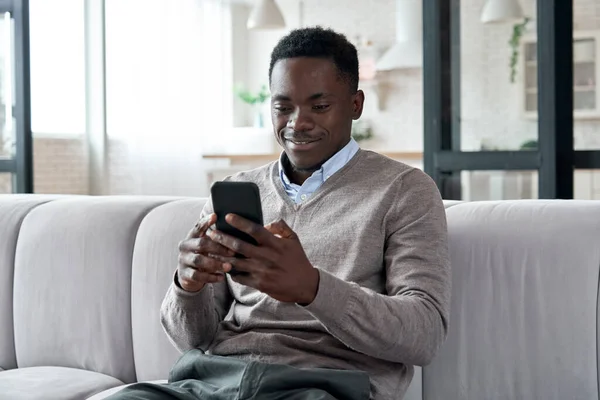 African american man using mobile apps sitting on couch at home.