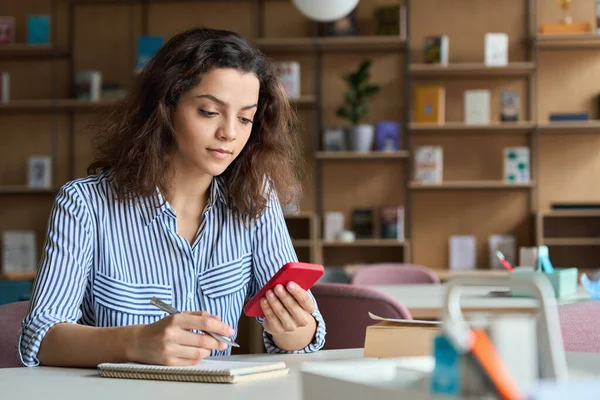 Hispanic latin girl college student holding smartphone studying in university.