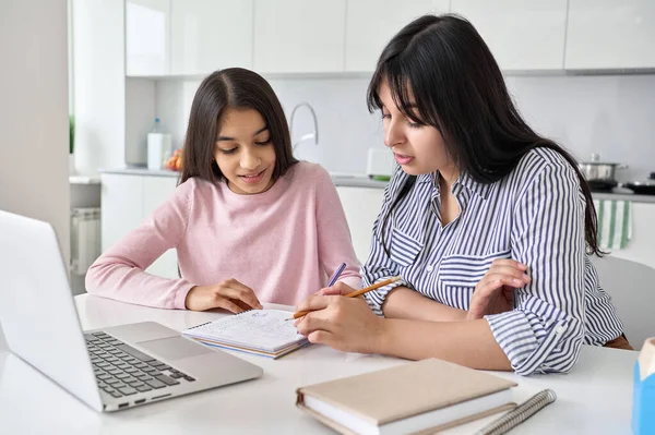 Young indian mother helping teen daughter remote studying at home.