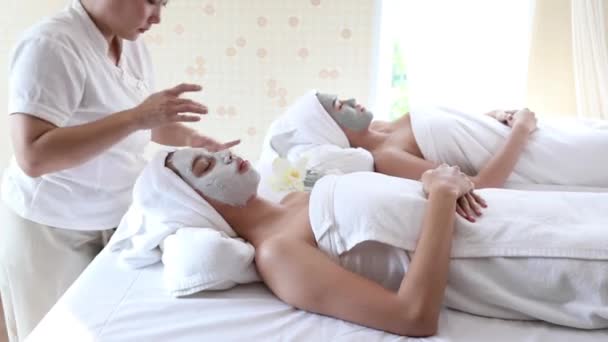美容師は若いアジアの女性の頬に顔のマスクをこすりつけるために指を使用します Vdoズームでハンドヘルド — ストック動画