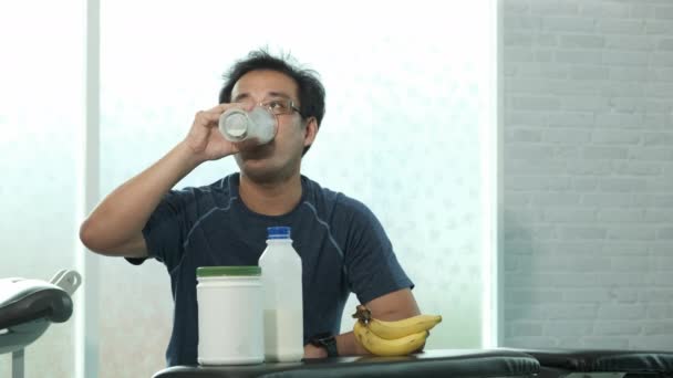 若いアジアのスポーツマンは ジムでのウェイトトレーニングの後 牛乳を飲み ベンチに空のガラスを置きます スポーツ ボディービル フィットネス 人々のコンセプト — ストック動画