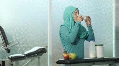 Yeşil tesettürlü genç kadın Müslümanlar, spor salonundaki ağırlık çalışmalarından sonra süt içip boş bardakları bankın üzerine koyuyorlar. spor, vücut geliştirme, spor ve insan konsepti
