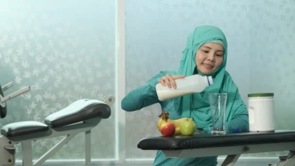 緑のヒジャーブの若い女性ムスリムたちがフィットネスルームのベンチで牛乳をグラスに注いでいます スポーツ ボディービル フィットネス 人々のコンセプト — ストック動画