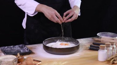 Genç Asyalı Aşçı ekmek yapmak için hamur karıştırmadan önce ekmeğin içine dört yumurta koyup kırıyor.