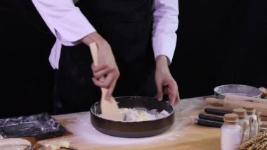 Genç Asyalı Aşçı elinde spatula ile peynirli ekmeği karıştırıyor dört kasede ekmek yapmak için hamur karıştırıyor.