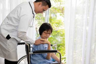 Parlak bir pencerenin yanında tekerlekli sandalyede oturan, empati, sağlık ve rehabilitasyon desteğini temsil eden bir kadını tedavi eden bir doktor.