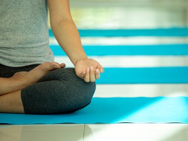 Mavi yoga minderinin üzerinde bağdaş kurmuş, sakin bir şekilde meditasyon yapan, sakin bir şekilde el hareketleriyle huzur ve huzur dolu, huzurlu bir ortamda iç dengeyi gösteren bir kadın.