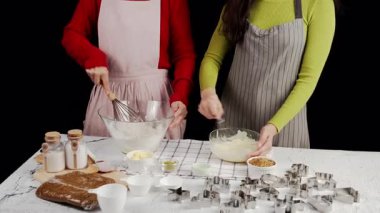 Kurabiye hamurunu birlikte hazırlayan iki kişi, pişirme aletleri ve kesicilerle çevrili cam kaselerde malzemeleri çırpma; sıcak ev yapımı pişirme atmosferi ve işbirlikçi mutfak