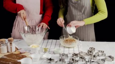 İki insan birlikte kurabiye hamuru hazırlıyor, pişirme aletleri ve kesicilerle çevrili cam kaseler içinde çırpıyor, sıcak bir mutfakta ev yapımı pişirme anı yakalıyor.