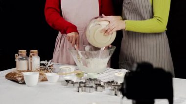 Önlüklü iki kadın kurabiye hamuru ve unu birleştiriyor, hamuru mutfak tezgahında pişirme malzemeleri, kurabiye keskisi ve aletlerle hazırlıyorlar.