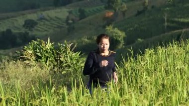 Güneş doğarken bir dağda verimli pirinç tarlalarında koşan Asyalı kadın tarım ortamında doğa, sağlık ve kırsal yaşam tarzının tadını çıkarıyor.