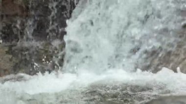 Doğal bir şelalenin yakın çekimi kayalık bir akıntıya sıçrıyor, doğal arka planlar için tatlı su ve beyaz köpük sergiliyor, rahatlama ve sağlıklılık görselleri.