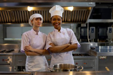 Profesyonel şefler, ticari bir mutfakta çapraz kollarla poz vererek güven takım liderliğini ve aşçılık profesyonelliğini ifade ederler.