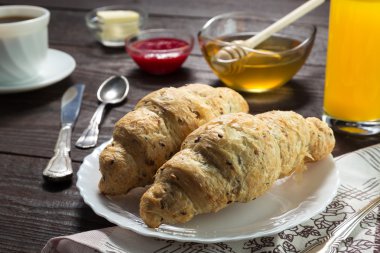 Nefis bir kahvaltı. Bal, reçel, kruvasan, kahve, bıçak, çatal, kaşık, portakal suyu, pastırma, tereyağı, jambon ile servis edilir. Tahta masa..