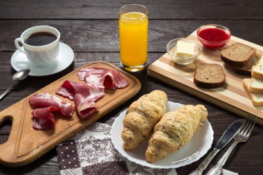 Nefis bir kahvaltı. Bal, reçel, kruvasan, kahve, bıçak, çatal, kaşık, portakal suyu, pastırma, tereyağı, jambon ile servis edilir. Tahta masa..