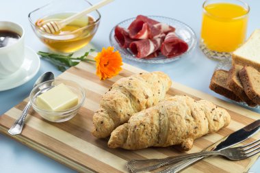 Nefis bir kahvaltı. Tereyağı, portakal suyu, reçel, bal, kruvasan, bıçak, çatal ile servis edilir. Sarı, mavi. Mavi arkaplan