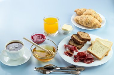 Nefis bir kahvaltı. Tereyağı, portakal suyu, reçel, bal, kruvasan, bıçak, çatal ile servis edilir. Sarı, mavi. Mavi arkaplan