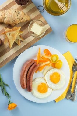 Nefis bir kahvaltı. Tereyağı, portakal suyu, reçel, bal, kruvasan, bıçak, çatal ile servis edilir. Sarı, mavi. Mavi arkaplan.