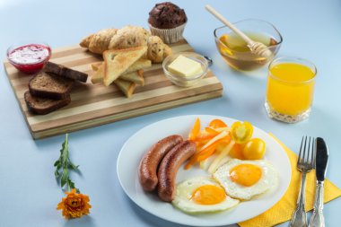 Nefis bir kahvaltı. Tereyağı, portakal suyu, reçel, bal, kruvasan, bıçak, çatal ile servis edilir. Sarı, mavi. Mavi arkaplan.