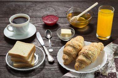 Nefis bir kahvaltı. Bal, reçel, kruvasan, kahve, bıçak, çatal, kaşık, portakal suyu, pastırma, tereyağı, jambon ile servis edilir. Tahta masa..