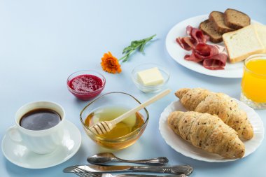 Nefis bir kahvaltı. Tereyağı, portakal suyu, reçel, bal, kruvasan, bıçak, çatal ile servis edilir. Sarı, mavi. Mavi arkaplan