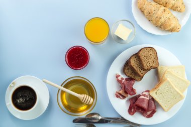 Nefis bir kahvaltı. Tereyağı, portakal suyu, reçel, bal, kruvasan, bıçak, çatal ile servis edilir. Sarı, mavi. Mavi arkaplan