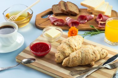 Nefis bir kahvaltı. Tereyağı, portakal suyu, reçel, bal, kruvasan, bıçak, çatal ile servis edilir. Sarı, mavi. Mavi arkaplan