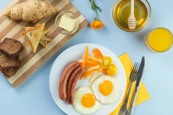 Nefis bir kahvaltı. Tereyağı, portakal suyu, reçel, bal, kruvasan, bıçak, çatal ile servis edilir. Sarı, mavi. Mavi arkaplan.