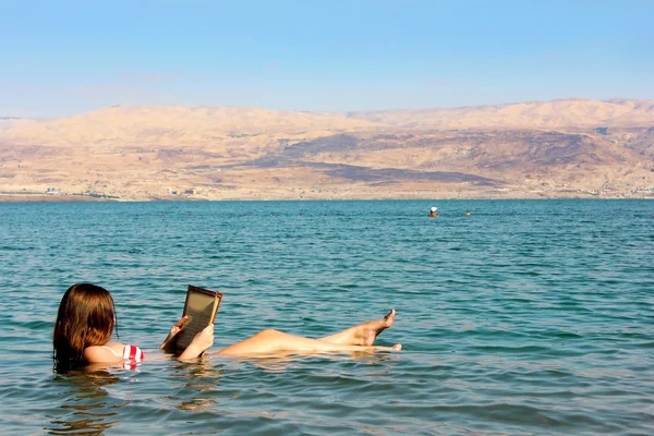 Fiatal nő elolvassa a könyvet, a Holt-tenger Izrael úszó — Stock Fotó
