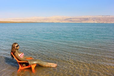 tedavi edici çamurlar ile bulaşmış kız sunbathes, ölü deniz