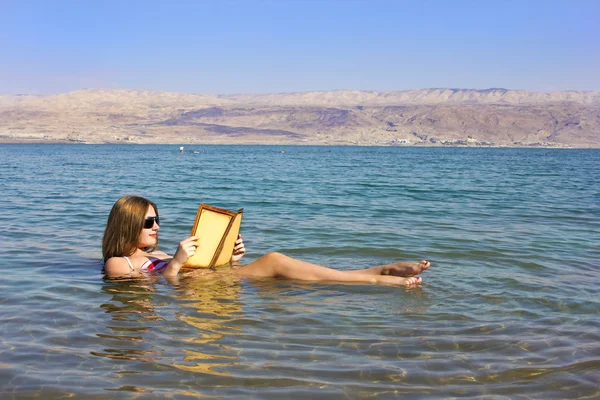 Ung flicka läser en bok som flyter i döda havet i Israel Stockfoto