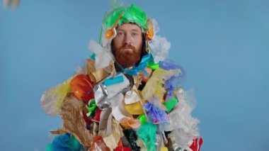 Plastik ve diğer çöpler çöp kostümü giymiş adamın üzerine düşüyor. Kameraya bakıyorum. Yavaş çekim.