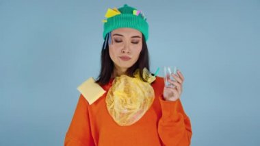 Üzerinde çöp olan Asyalı kadın plastik bardaktan su içip onu fırlatıyor. Kameraya bakıyorum..