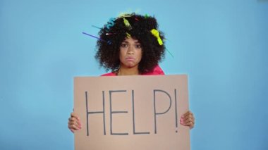 Saçında plastik çöp olan mutsuz bir kadın. Elinde karton levha, üstünde de yazı var..