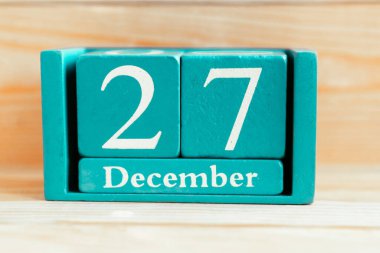 27 Aralık. Ahşap zemin üzerinde ay ve tarih olan mavi küp takvimi.