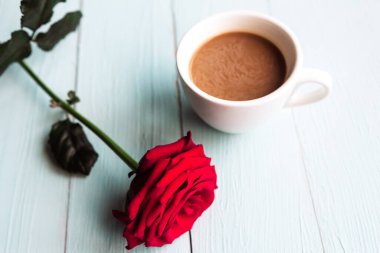 Kırmızı gül ve kahve fincanı ahşap masada, üst manzara.