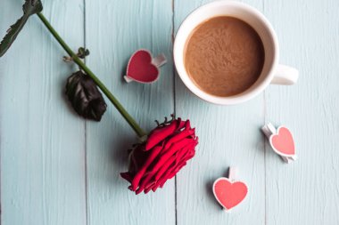 Kırmızı gül ve kahve fincanı ahşap masada, üst manzara.