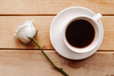 Kahve fincanı ve ahşap arka planda beyaz gül.