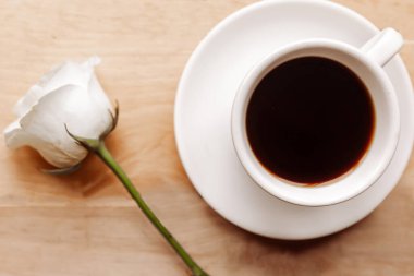 Kahve fincanı ve ahşap arka planda beyaz gül.