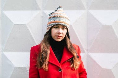 Örgü şapkalı güzel esmer kız portresi, beyaz tuğla duvar arka planı.