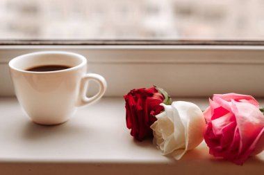 Kahve fincanı ve güller pencere eşiğinde, yakın plan.