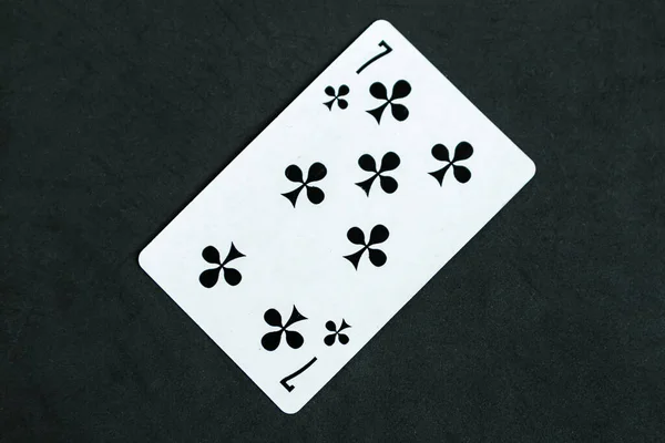 Seven of Clubs playing card, black background, top view