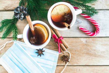 Coronavirus Noel 'i. Sıcak şarap, tıbbi maskeler ve Noel süslemeleri ahşap masa, üst manzara.